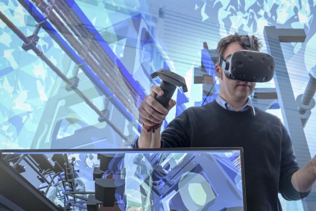 An operator wearing VR goggles is using controls to remotely control a robot.