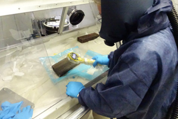 A scientist with protective clothing works on a sample.