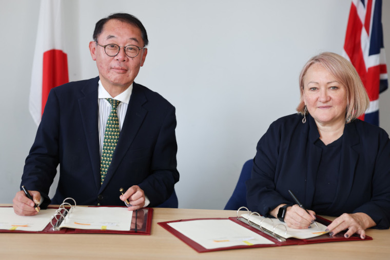 Kerry McCarthy, Parliamentary Under-Secretary of State (Minister for Climate) and Hiroshi Masuko, Senior Deputy Minister of Education, Culture, Sports, Science and Technology, signing the Memorandum of Cooperation on fusion energy in from t of the flags of Japan and the United Kingdom.