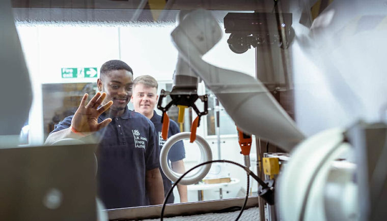 Apprentices at UKAEA working in a laboratory with a robotic arm.