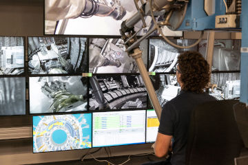 A robotics operator working in front of a bank of screens.