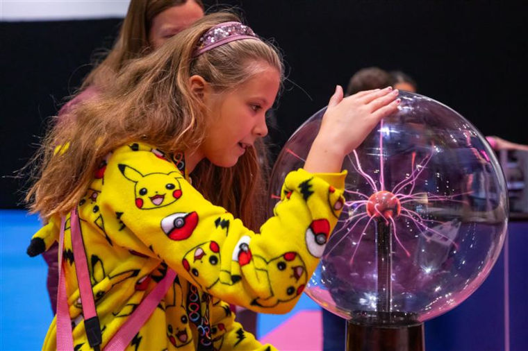 A girl with her hands on a plasma globe, fascinated by the plasma.