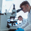 An expert in a white lab coat looking into a microscope at a facility at the UK atomic Energy Authority.