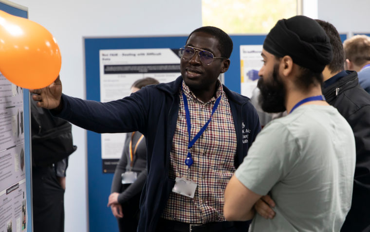 An expert from the UK Atomic Energy Authority explains opportunities in fusion energy to s student. He is pointing to a display board at a graduate showcase.