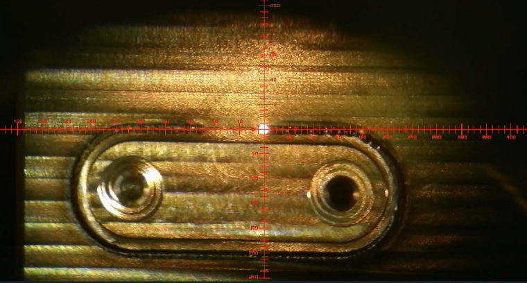 A close up through a microscope of specialist welding at the UK Atomic Energy Authority. There is an area of metal with a crosshairs target - in the middle is a bright dot from the electron beam welding.