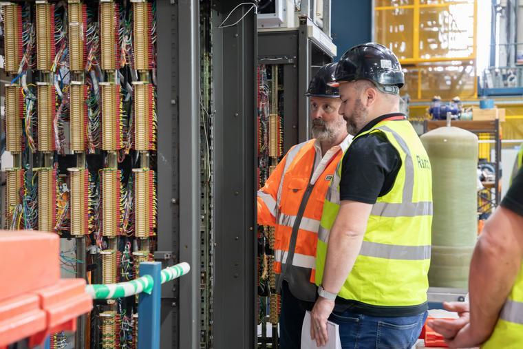 Experts from Ramco (UK) and the UK Atomic Energy Authority discussing asset based decommissioning in front of some large racks of fusion energy machine equipment.