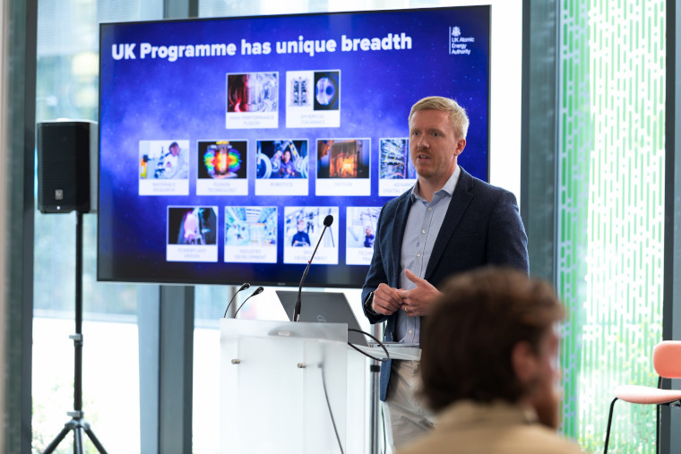 An expert presenter in front of a slide titled UK programme has unique breadth.