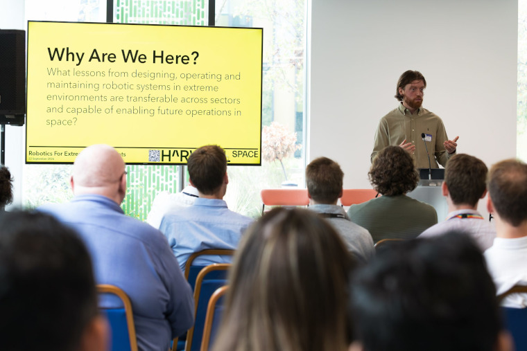 A presenter in front of a slide titled Why are we here?